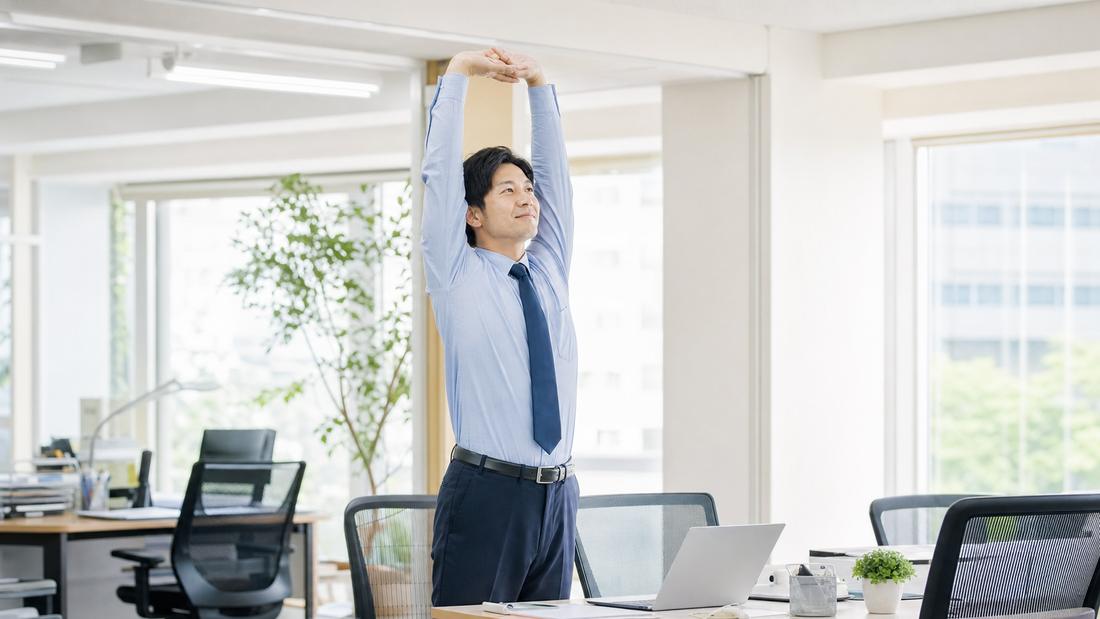 デスクで立ち上がり伸びをする社員のイメージ